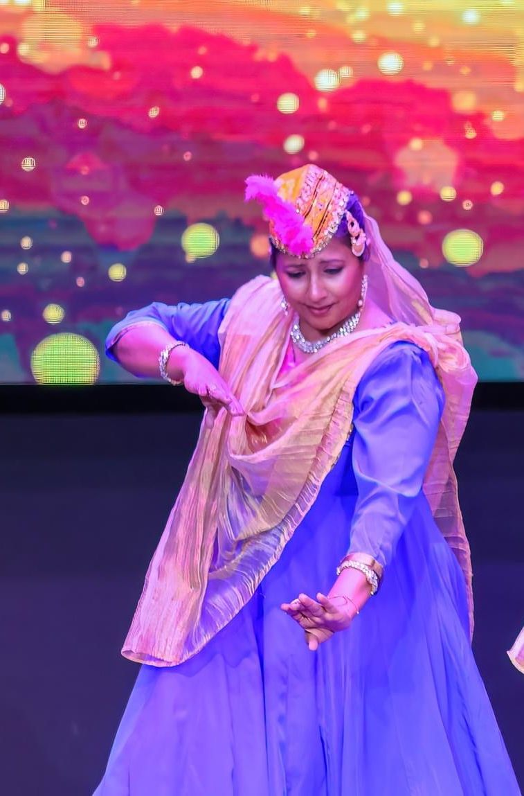Aarti Gupta performing Kathak on stage in blue anarkali with colorful backdrop