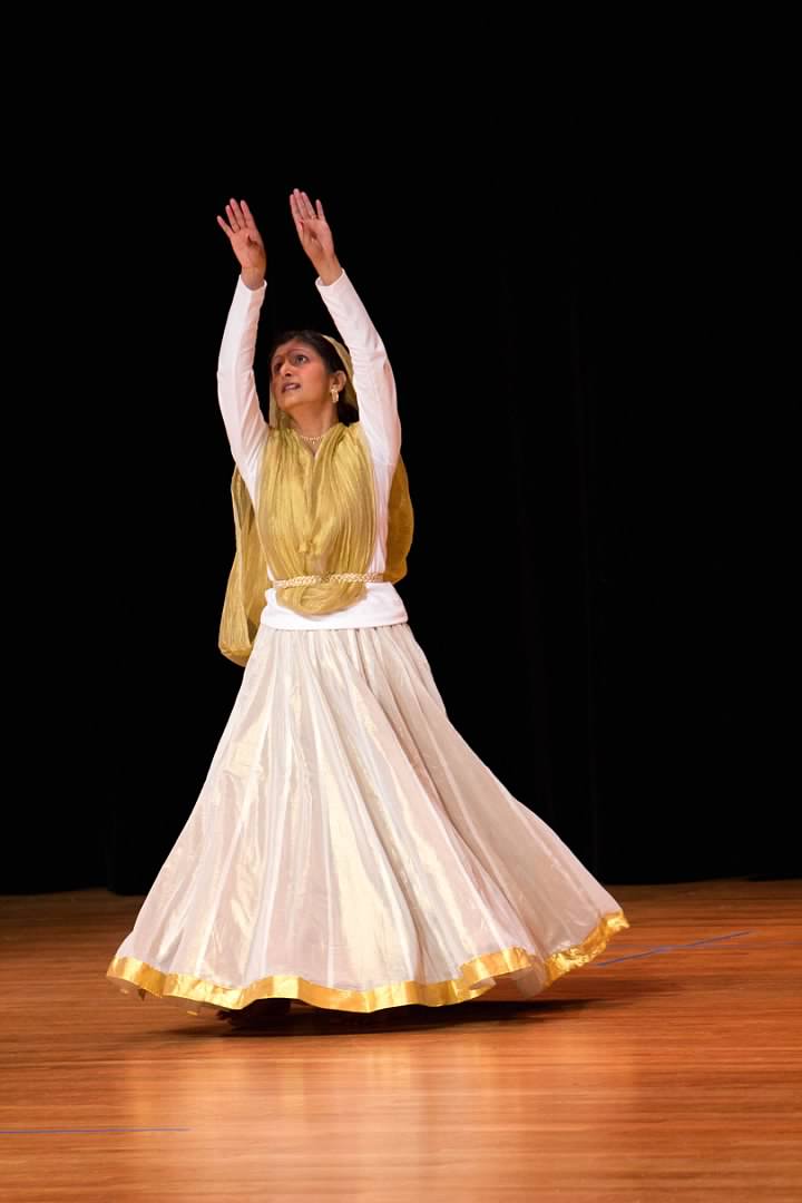 Sapna Adhikari performing Kathak on stage in white and gold attire